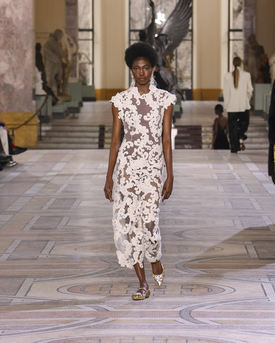 Or model on the runway at Paris fashion week wearing a cream gown with exaggerated ruffle shoulder