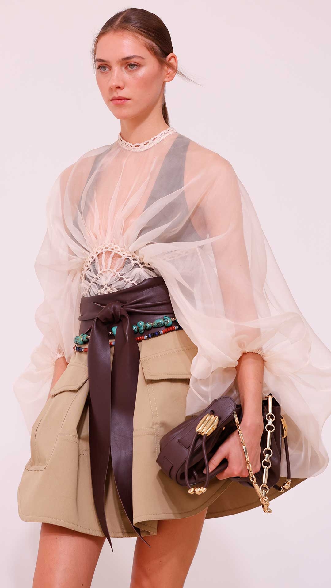 Look 25: Illuminate Macrame Bodice in Cream, Illuminate Cargo Mini Skirt in Sand, Mellow Stone Necklace in Gold/Multi, Halcyon Chain Belt in Copper Patina, Foam Wrap Belt in Coffee, Halcyon Clutch in Coffee and Goldie Gladiator in Espresso 