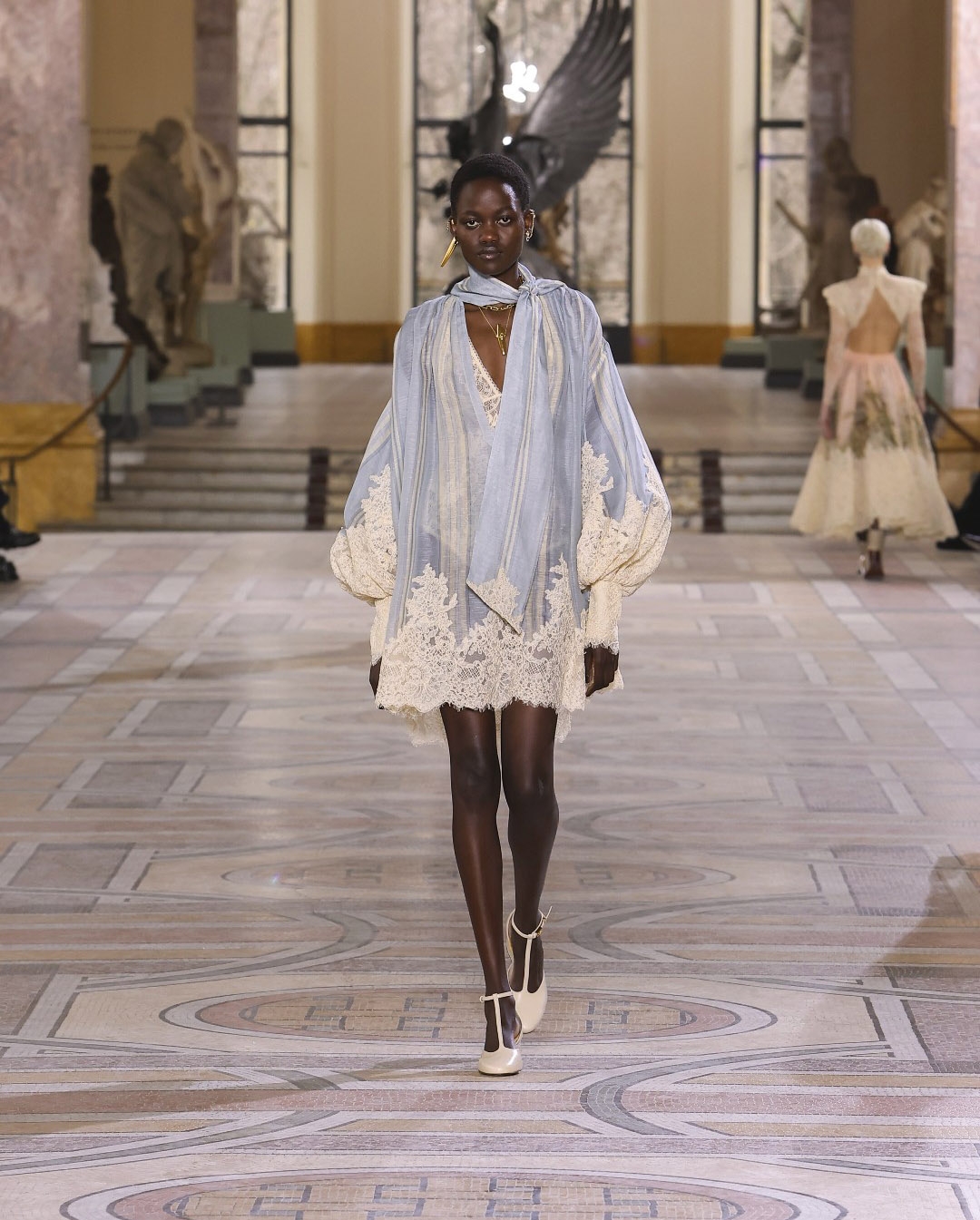 Or model on the runway at Paris fashion week wearing a cream gown with exaggerated ruffle shoulder
