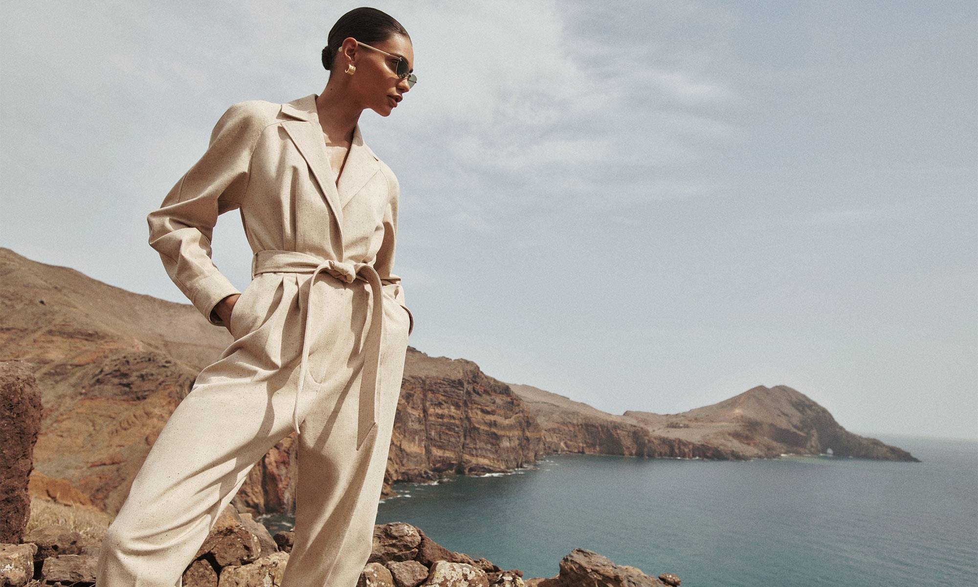Model wears the Natura Melange Jumpsuit in Natural, Zimmermann Laurel Hoops in Gold and Zimmermann Celeste Cat Eye in Bottle Green 