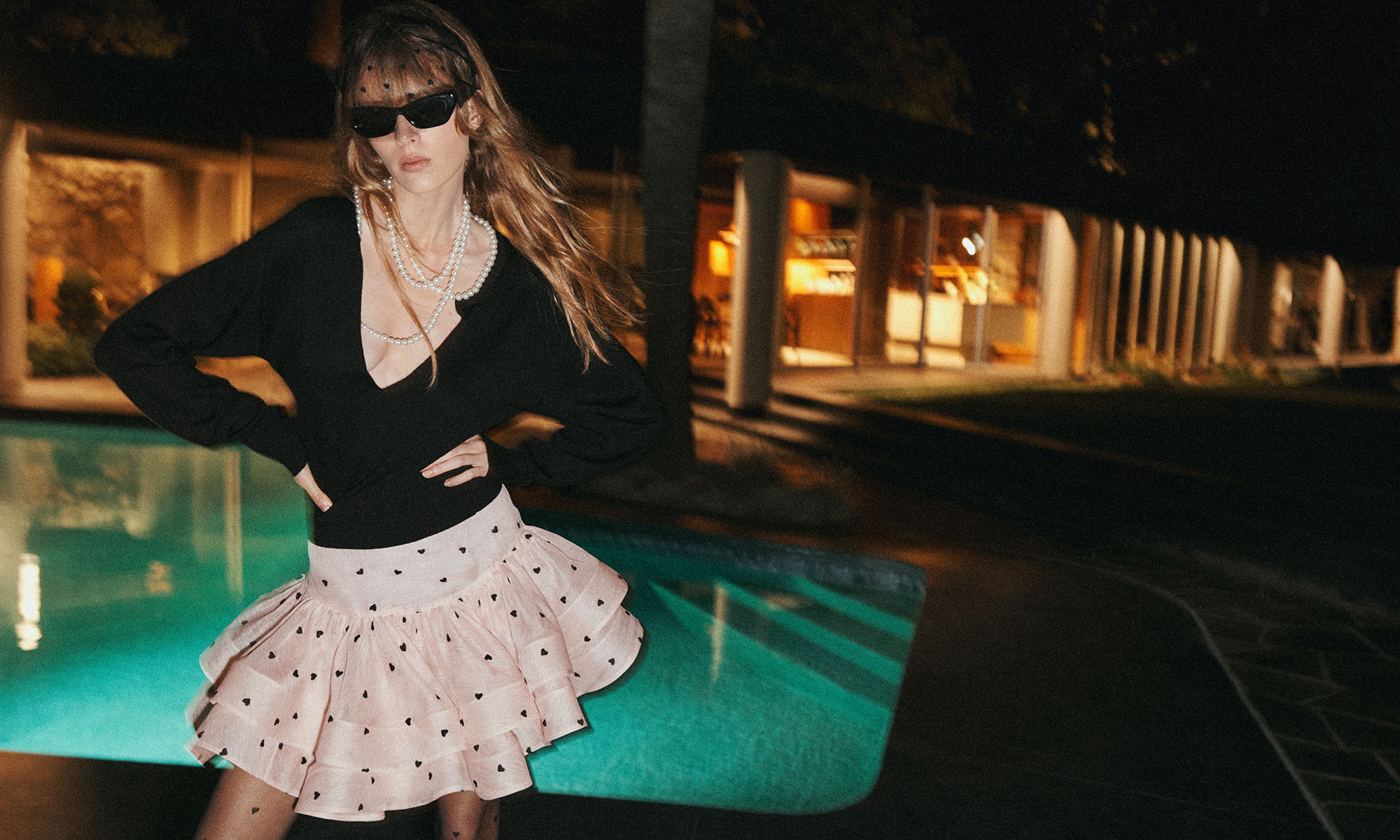 Model wears the CRUSH NECKLACE SWEATER IN BLACK, CRUSH FLIP MINI SKIRT IN PINK HEARTS, VEIL HEADBAND IN BLACK, ZIMMERMANN TUX MULE 65 IN BLACK AND Zimmermann Liv Square IN Black 