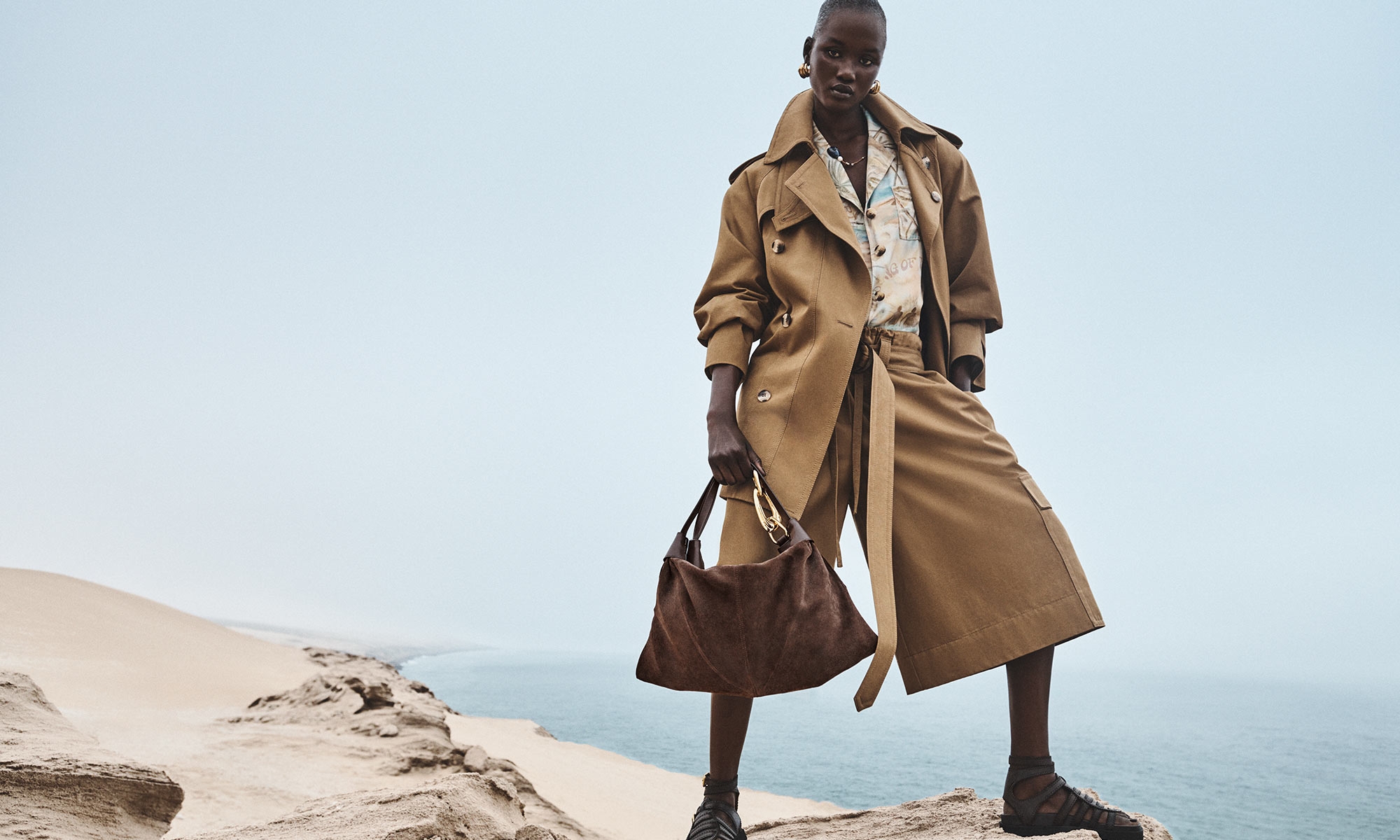 Model wears the Illuminate Bermuda Short in Khaki, Illuminate Anorak Jacket in Khaki, Illuminate Short Sleeved Shirt in Blue Morning, Mellow Stone Beaded Necklace in Gold/Multi, Glaze Hoops in Gold, Trampoline Hobo in Coffee and Goldie Gladiator 