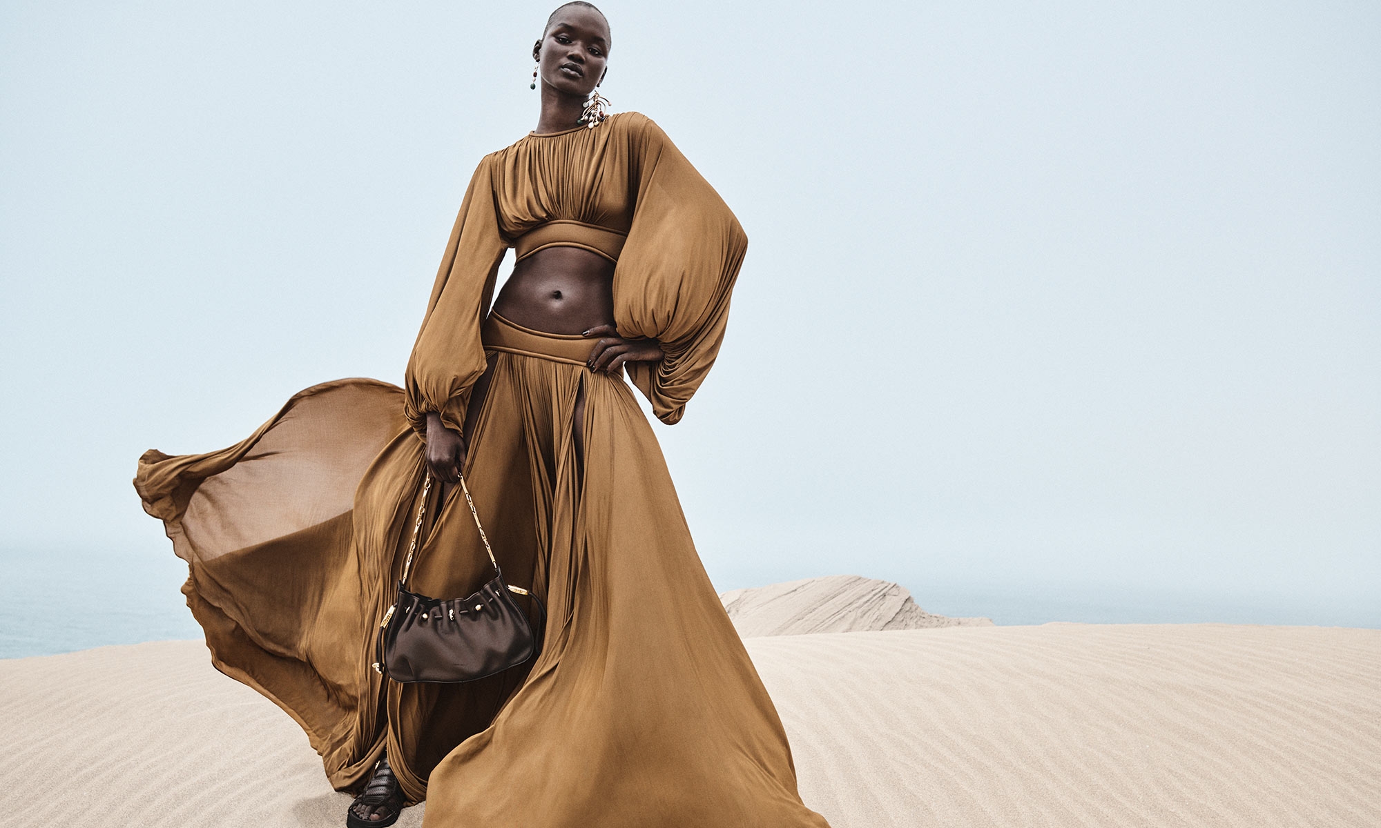 Model wears the Illuminate BATWING BODICE IN KHAKI, Illuminate MAXI SKIRT IN KHAKI, GOLDIE GLADIATOR IN ESPRESSO, HALYCON CLUTCH IN COFFEE AND MELLOW CHANDELIERS IN GOLD/MULTI 